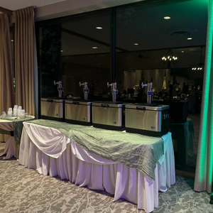 Event setup with tables, chairs, and a green curtain in a room.