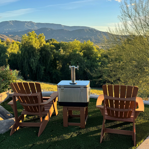 Two wooden chairs and a small table with a grill on a grassy area with mountains in the background.